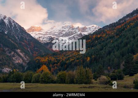 Maestose vette innevate si innalzano sopra un vivace arazzo di colori autunnali nella valle del Bujaruelo, nella regione di Ordesa, nei Pirenei. Foto Stock