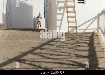 Un musicista maschile si trova in un vicolo luminoso, suona il clarinetto, con l'ombra dello strumento che scaglia a terra. Foto Stock
