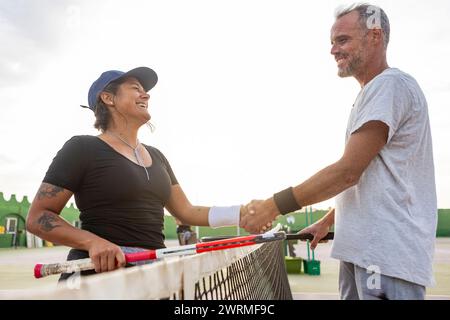 Due allegri tennisti, un uomo e una donna, stringono la mano sulla rete dopo la partita, mostrando sportività e gioia. Foto Stock