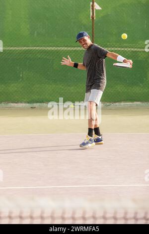Un uomo gioca a tennis su un campo all'aperto, guardando lontano dalla telecamera mentre si prepara a colpire la palla. Foto Stock