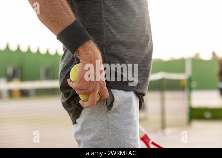 Vista laterale della vista ravvicinata di un tennista maschile corta e irriconoscibile mentre si afferra le palle da tennis dietro la schiena, preparandosi a servire durante una partita, ingegno Foto Stock