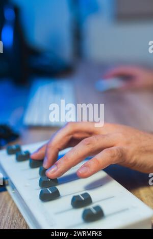 Le mani di una persona irriconoscibile ritagliate regolano meticolosamente le manopole di un mixer durante una sessione di registrazione in studio, con particolare attenzione alla produzione musicale Foto Stock