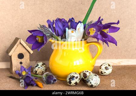 fiori primaverili in brocca gialla e uova di quaglia su fondo di legno Foto Stock