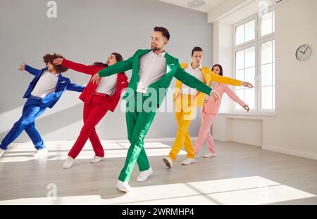 Gruppo di persone eleganti in abiti da lavoro colorati ballando allegramente. Gli uomini e le donne in abiti da lavoro colorati ballano con eleganza in abiti vivaci Foto Stock