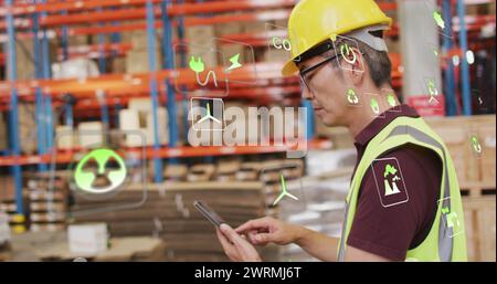 Immagine di icone ecologiche ed elaborazione dei dati su un uomo birazziale che lavora in magazzino Foto Stock