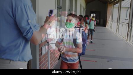 Immagine della cellula del coronavirus con gli scolari mascherati che disinfettano le mani prima della lezione Foto Stock