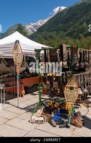 Vecchio equipaggiamento da sci e campane in vendita al mercato di strada con le montagne Aiguilles du Dru sullo sfondo in estate, Chamonix, Francia Foto Stock