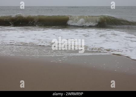 Onde con creste bianche inondare la spiaggia sabbiosa Foto Stock