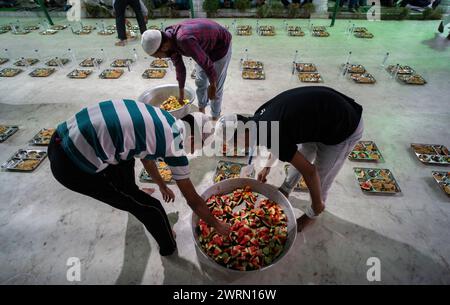 I volontari distribuiscono e organizzano file di pasto "iftar" per i devoti per rompere il digiuno, durante il mese sacro del Ramadan, a Burha Jame Masjid, il 13 marzo 2024 a Guwahati, Assam, India. Crediti: David Talukdar/Alamy Live News Foto Stock