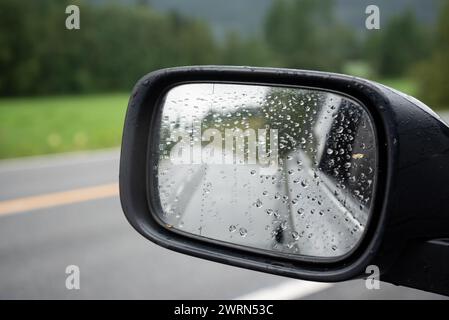 Specchietto retrovisore laterale di un'auto nera ricoperta di gocce d'pioggia in una giornata autunnale bagnata. Foto Stock