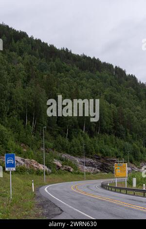 autostrada con una curva stretta a destra ai piedi delle montagne ricoperte di alberi verdi in una giornata nebbiosa. Foto Stock