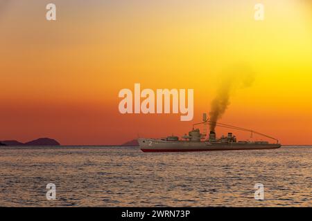 Nave da guerra in mare vicino alla riva al tramonto Foto Stock
