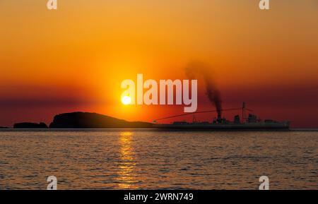 Nave da guerra in mare vicino alla riva al tramonto Foto Stock