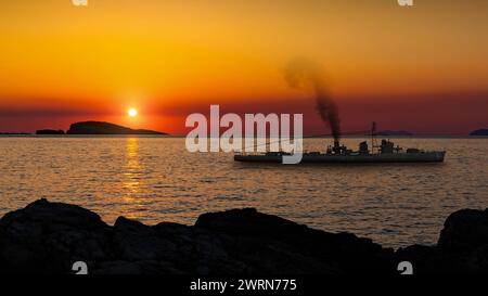 Nave da guerra in mare vicino alla riva al tramonto Foto Stock