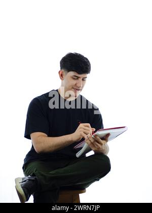 Un giovane che si muove felicemente in un taccuino, rilassato di fronte a sfondo bianco. Perfetto per concetti di produttività, creatività e benessere professionale Foto Stock