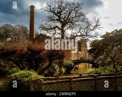 Packhorse Bridge che attraversa il fiume Bollin con Quarry Bank Mill in lontananza. Wilmslow, Cheshire. REGNO UNITO Foto Stock