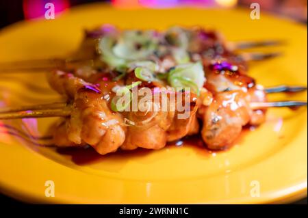 Spiedini di legno con pezzi di filetto di pollo in salsa teriyaki dalla griglia serviti al ristorante yakitori di Milano, in Italia, da vicino Foto Stock