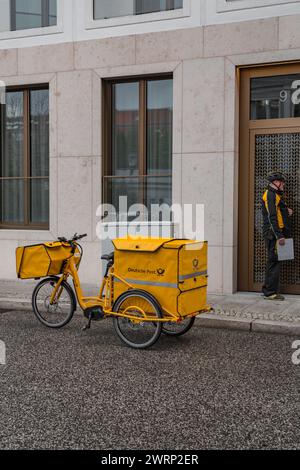 Berlino, Germania - 16 dicembre 2021: Corriere senior che consegna la posta in bicicletta, dipendente di Deutche Post, il servizio postale tedesco. Foto Stock