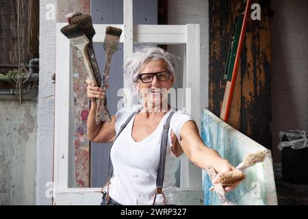 sorridente ridendo felice donna anziana matura ritratto, orgogliosa artista, sulla cinquant'anni con capelli grigi e occhiali neri, con un gesto positivo persuasivo Foto Stock