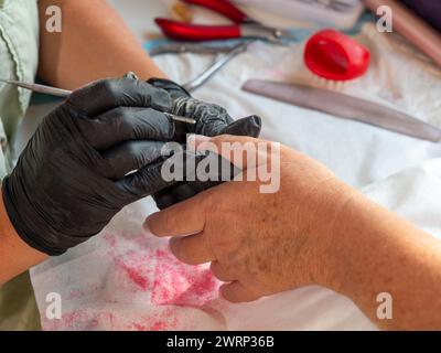 Donna di manicure che rimuove le cuticole con un prodotto per la rimozione delle cuticole per la vernice permanente delle unghie Foto Stock