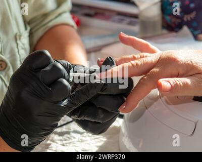 Donna che fa la manicure applicando lo smalto francese per la pittura permanente delle unghie Foto Stock