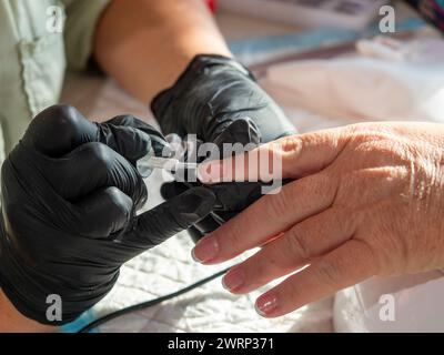 Donna che fa la manicure applicando lo smalto francese per la pittura permanente delle unghie Foto Stock