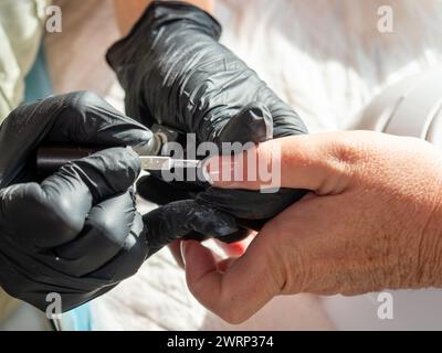 Donna che fa la manicure applicando lo smalto francese per la pittura permanente delle unghie Foto Stock