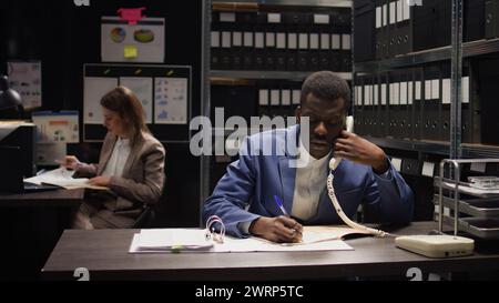 Il poliziotto nero conduce un'indagine discreta, analizza le prove e fa importanti telefonate. L'ufficiale di legge afroamericano raccoglie dichiarazioni di testimoni e informazioni riservate per telefono. Foto Stock