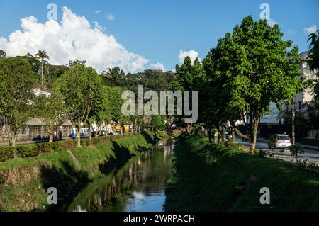 Vista del canale d'acqua del fiume Piabanha che scorre tra Tiradentes avenue nel quartiere Centro sotto il cielo nuvoloso soleggiato del pomeriggio estivo. Foto Stock