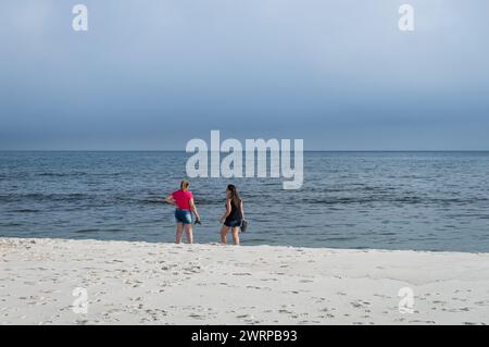 Due donne in piedi sulla spiaggia vuota di Praia Seca nelle acque blu dell'Oceano Atlantico vicino alla via Sao Judas Tadeu sotto il cielo nuvoloso pomeridiano estivo. Foto Stock