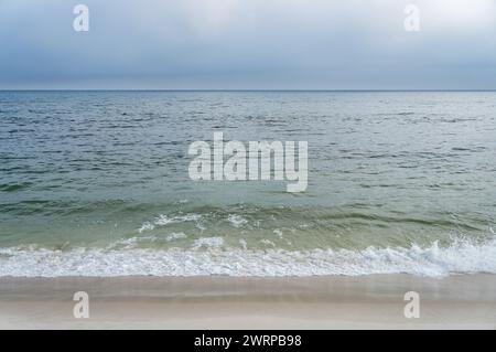 Onde calme dalle acque blu dell'Oceano Atlantico che colpiscono e lavano le sabbie bianche della spiaggia di Praia Seca sotto il cielo nuvoloso del pomeriggio estivo. Foto Stock