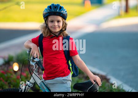 Bambino in bicicletta nel parco estivo. I bambini guidano una bicicletta su un vialetto esterno. I bambini vanno in bicicletta in città indossando i caschi. Bambino in bicicletta Foto Stock