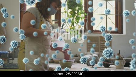 Immagine di cellule covid 19 sopra la donna che lavora in studio di ceramica indossando la maschera facciale Foto Stock