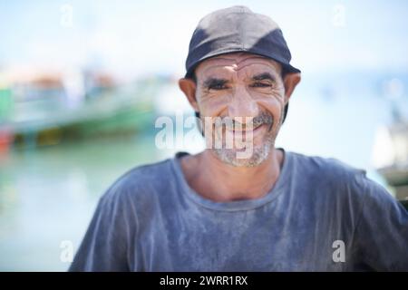 Pescatore, ritratto e uomo aspro con sorriso, porto e rughe dovute all'esposizione alla luce del sole. Barche, navi e acqua o pesca per lavoro in Brasile Foto Stock