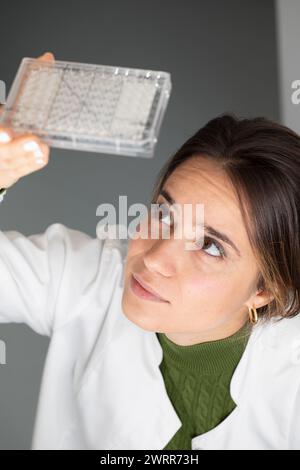 Ricercatrice specializzata che esamina una piastra di microtitolazione, lavori di laboratorio in corso Foto Stock