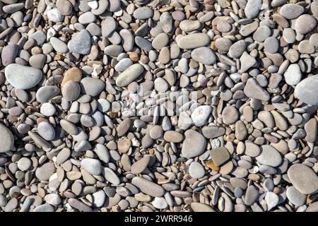 Ciottoli costieri grigi alla luce del sole, vista dall'alto, texture fotografica di sfondo ravvicinata di un terreno di spiaggia Foto Stock