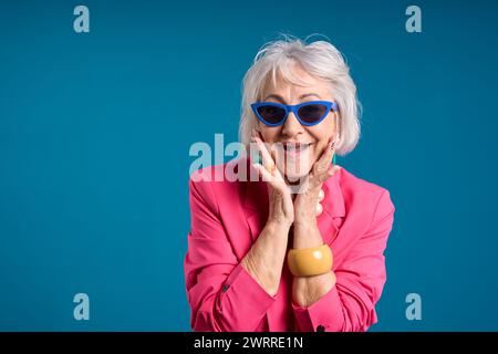 Vivace donna anziana con giacca rosa e occhiali da sole blu Foto Stock
