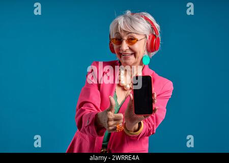 Donna anziana alla moda che regala pollice allo smartphone Foto Stock