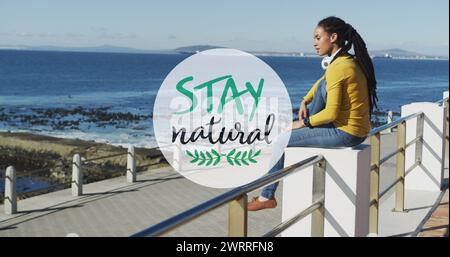 Rimani un banner naturale contro una donna afroamericana che indossa le cuffie sul lungomare Foto Stock