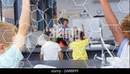 Immagine di icone chimiche su scolari diversi che alzano le mani in classe Foto Stock