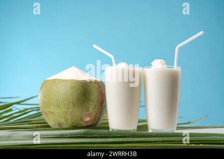 Un bicchiere di dolce profumo di cocco con acqua di cocco e sfondo blu. Foto Stock