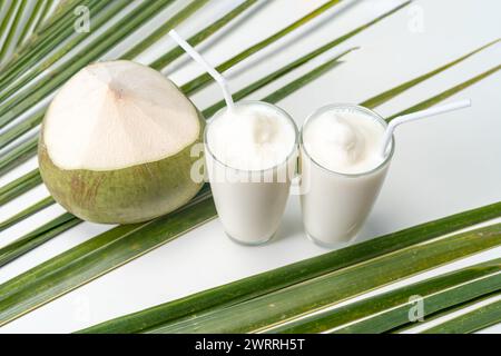 Un bicchiere di dolce profumo di cocco con acqua di cocco e sfondo blu. Foto Stock