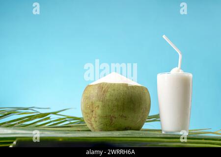 Un bicchiere di dolce profumo di cocco con acqua di cocco e sfondo blu. Foto Stock