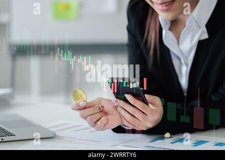 donna che tiene il bitcoin e guarda il cellulare. Donna che detiene la valuta cripto mobile e Bitcoin del diagramma grafico Foto Stock