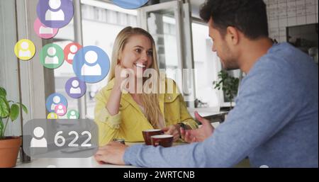 Immagine di icone dei social media che fluttuano sopra una felice coppia caucasica che parla e beve caffè Foto Stock