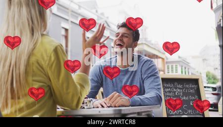 Immagine di icone del cuore che fluttuano sopra la felice coppia caucasica che parla e sorride Foto Stock