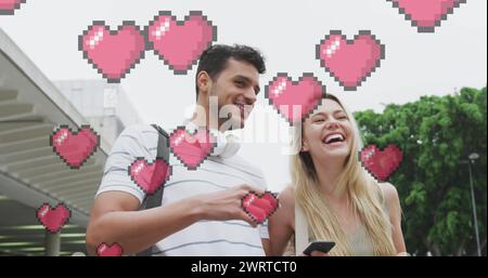 Immagine delle icone del cuore che fluttuano sopra una felice coppia caucasica che parla e usa lo smartphone Foto Stock