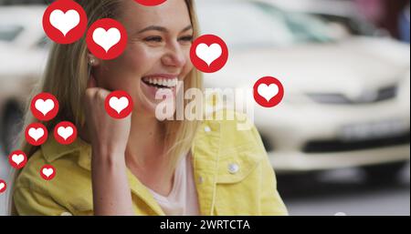 Immagine di icone del cuore che fluttuano sopra una donna caucasica sorridente e beve caffè Foto Stock