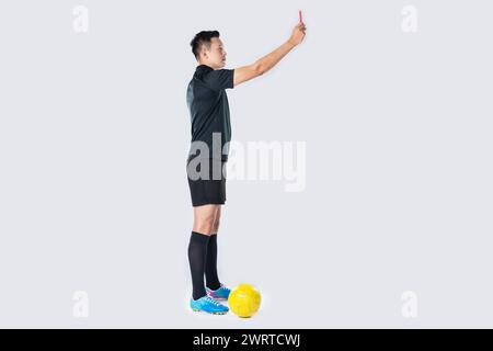 Ritratto a figura intera di un arbitro di calcio che dà un cartellino rosso isolato su sfondo bianco. Foto Stock