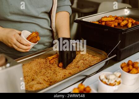 Donna che cucina deliziosi churros con panna e cioccolato in un caffè di strada. Dolce cibo spagnolo di strada. Foto Stock